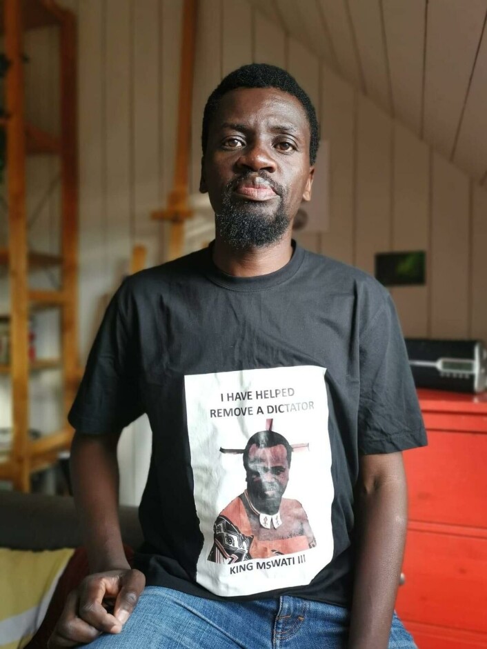 «Fjern diktatoren»: Bheki Dlamini i en T-skjorte som retter kritikk mot kongen i Eswatini. Han forteller om venner som har blitt fengslet for å gå med klær med regimekritiske budskap. «Fjern diktatoren»: Bheki Dlamini i en T-skjorte som retter kritikk mot kongen i Eswatini. Han forteller om venner som har blitt fengslet for å gå med klær med regimekritiske budskap.