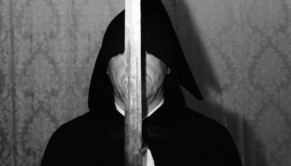 RIDDER: En anonym hettekledd mann, klar til å slå nye ordensmedlemmer til riddere.