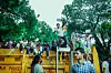 En folkemengde av unge mennesker sitter og står på en i en park i New Delhi.