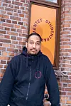 Person i svart hettegenser foran en rød murvegg og oransje dør.